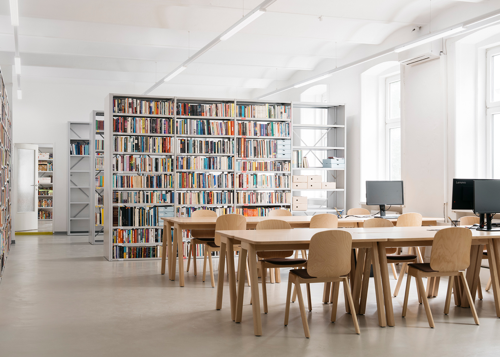 Moderne Bibliothek mit Regalen voller Bücher, Tischen und Computern für Lernende.