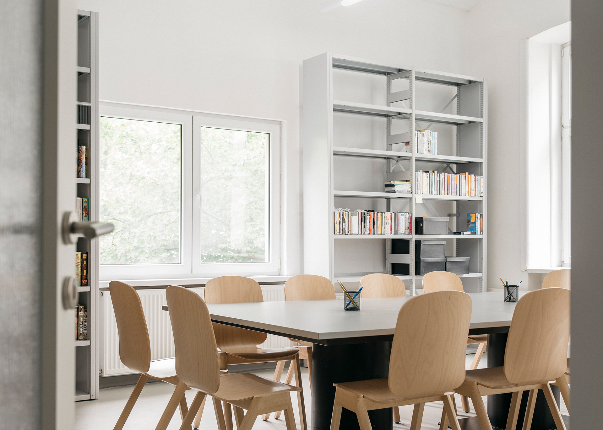 Heller Besprechungsraum mit einem großen Tisch, Stühlen und Bücherregalen.