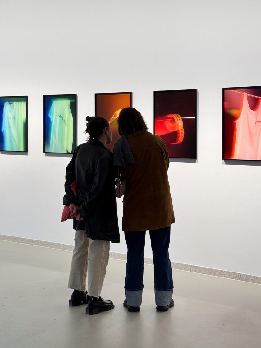 Two visitors admire colorful art pieces featuring clothing in a gallery setting.