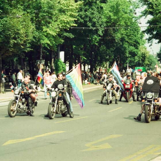 Motorcyclists parade in Vienna, waving flags during a vibrant celebration event.
