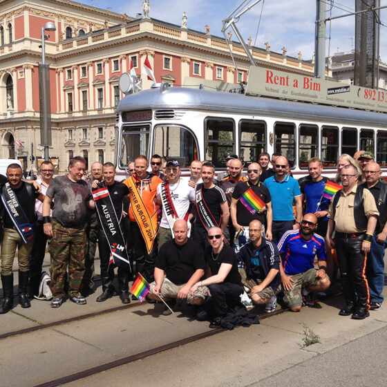 Group of diverse individuals celebrating Pride in Vienna, posing near a vintage tram.
