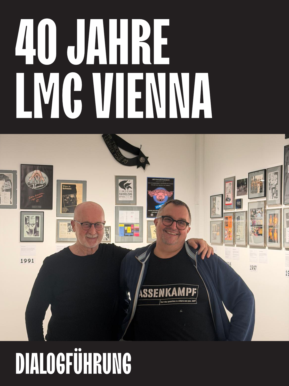 Two men pose together in front of a gallery wall celebrating 40 years of LMC Vienna.
