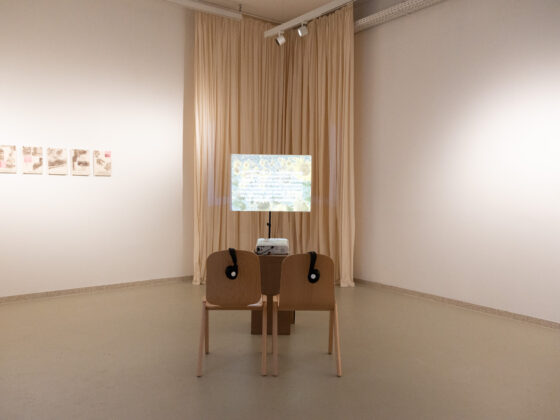 Art gallery featuring a sketch display with two chairs and headphones for audio.