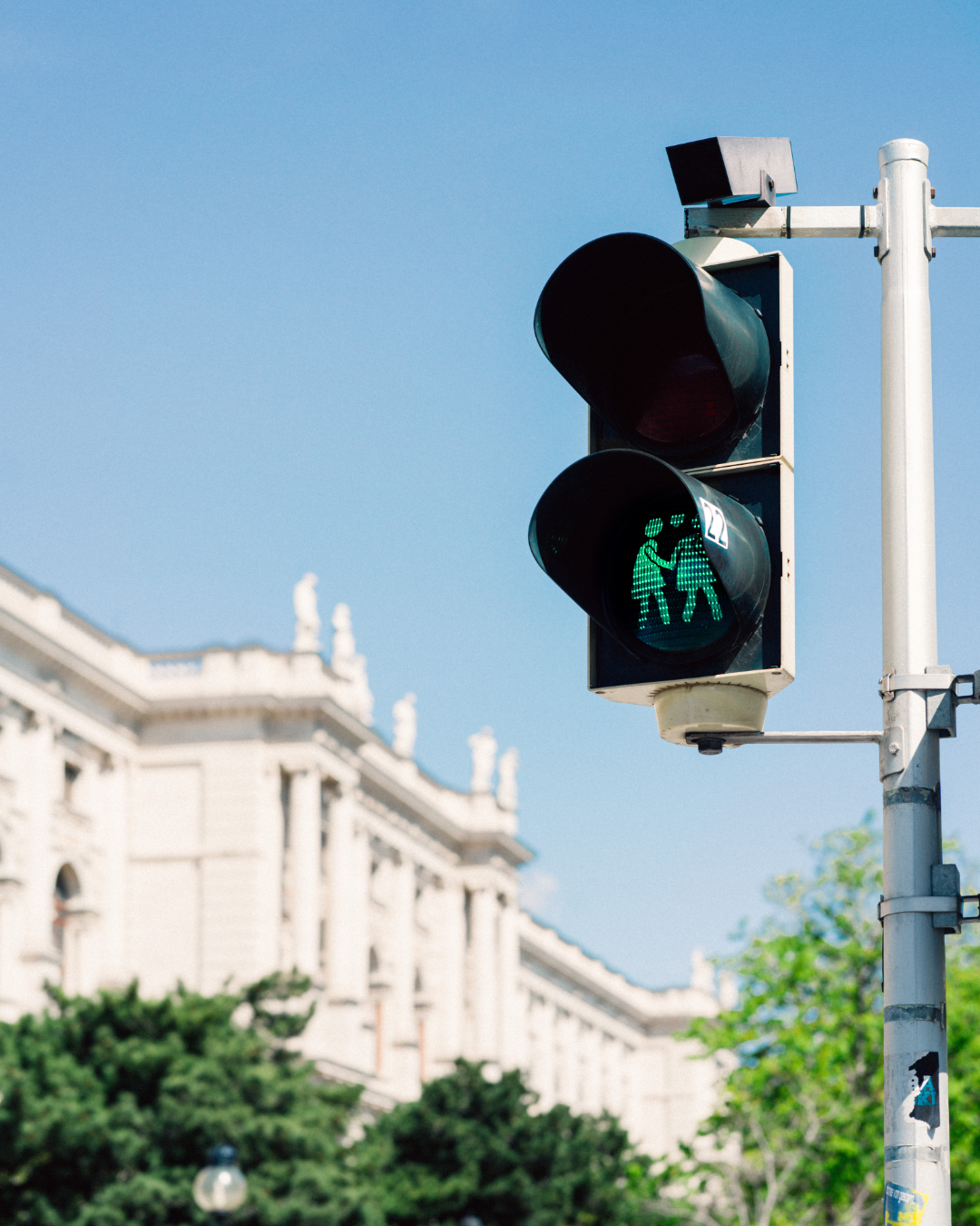 Grünes Ampelsignal zeigt Fußgänger, im Hintergrund ein Gebäude, sonniger Tag.