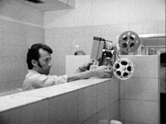 Person bedient einen Projektor in einem Raum mit weißen Fliesen am Nachmittag.